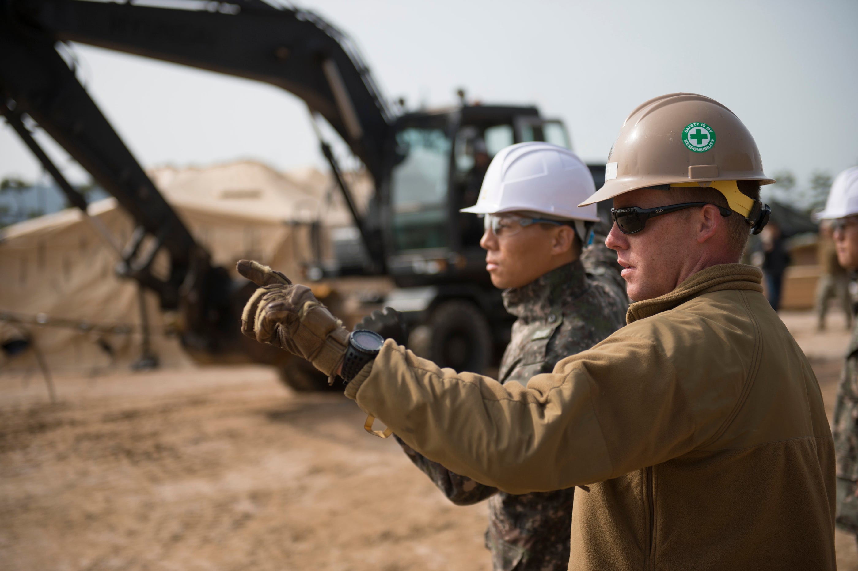 Two construction workers discussing a project with construction machinery in the background.