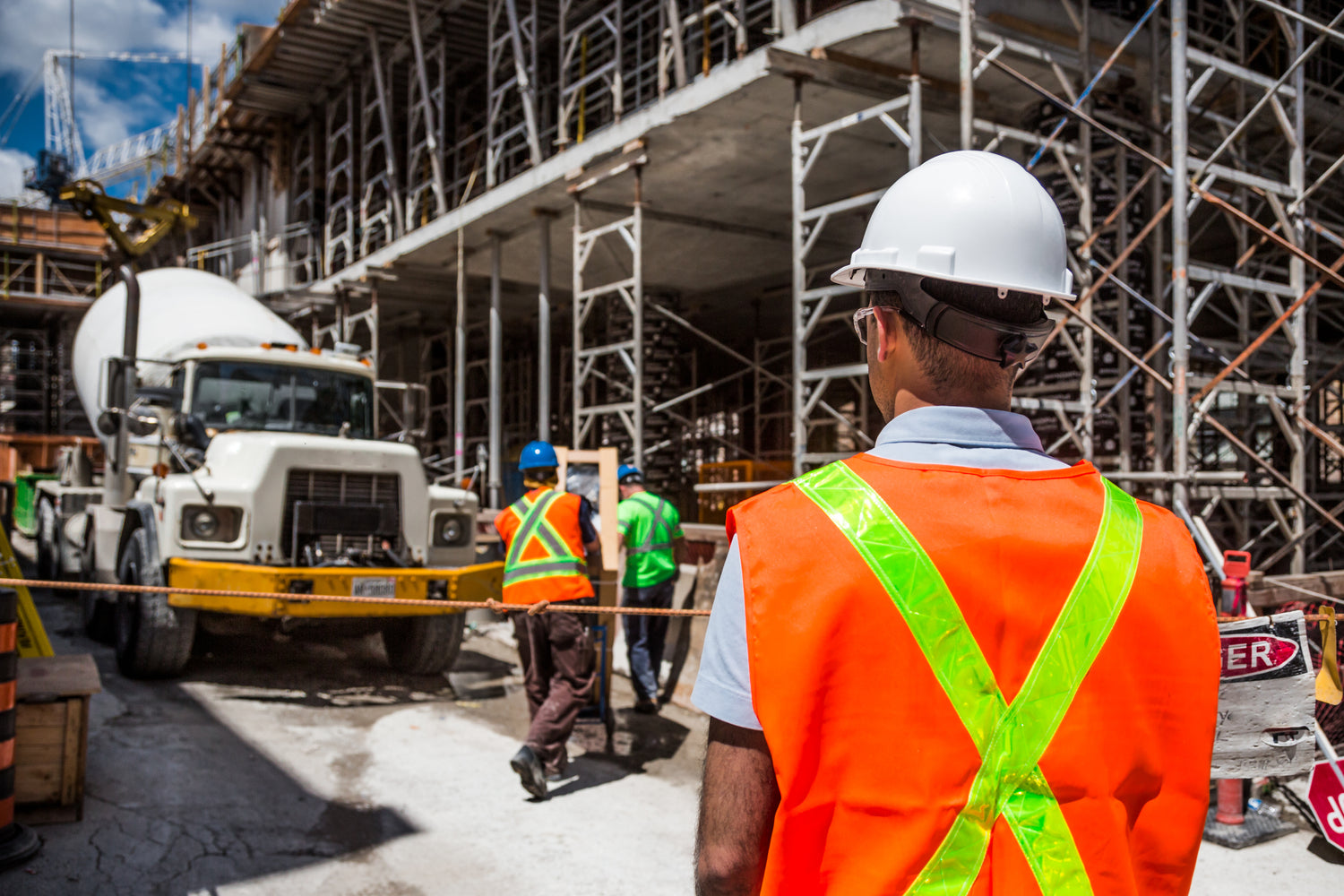 exterior shot of a construction site with a cement truck pouring cement and works standing nearby.